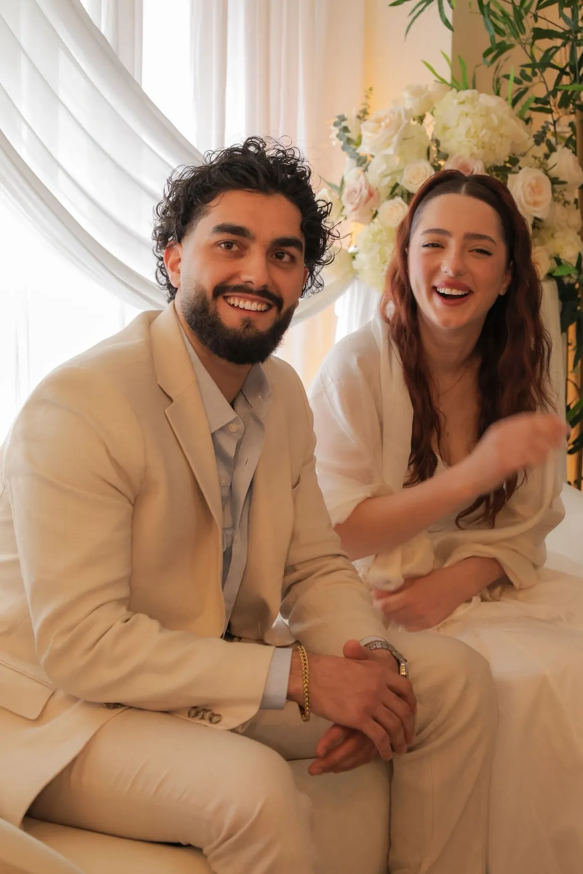 Couple smiling and laughing together in front of a white floral arrangement