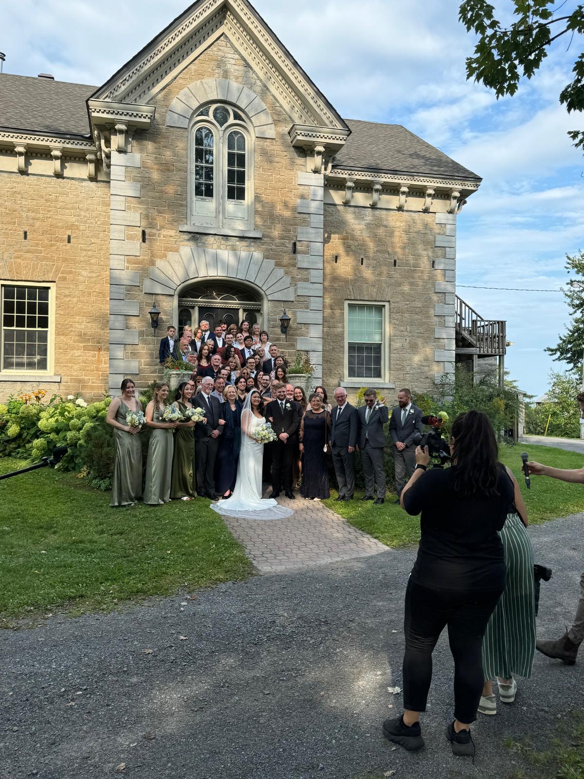 Group photo of the wedding party in front of a stone venue
